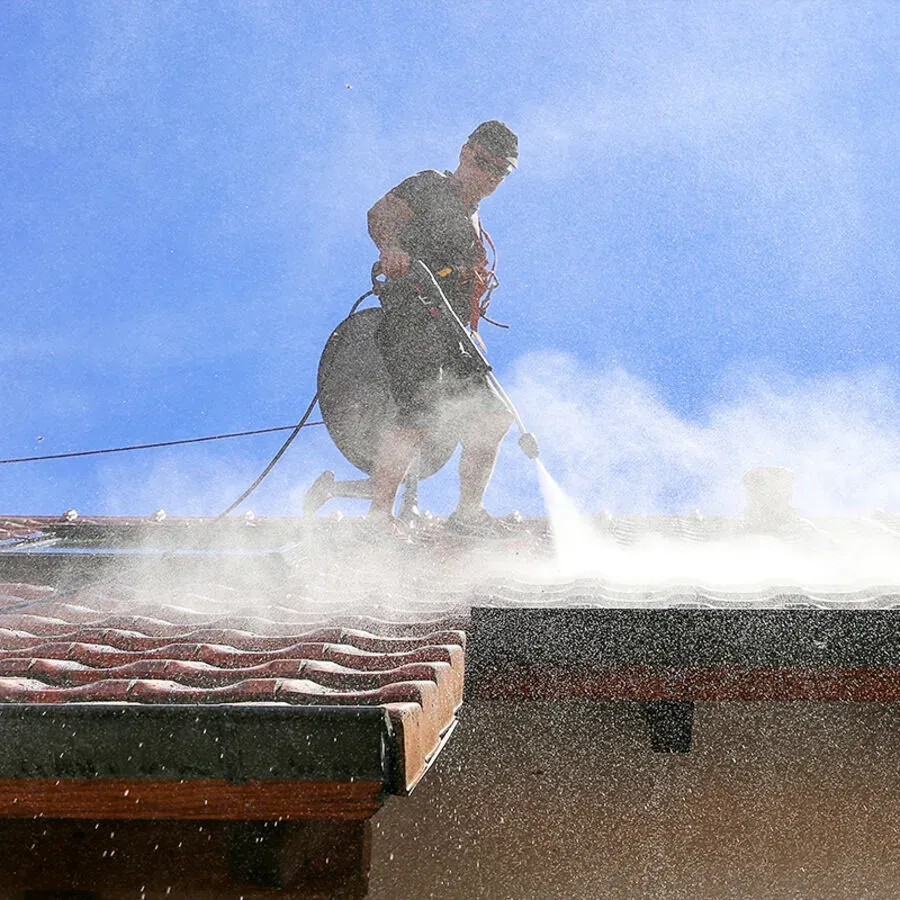 A man is cleaning a tiled roof with a high pressure washer