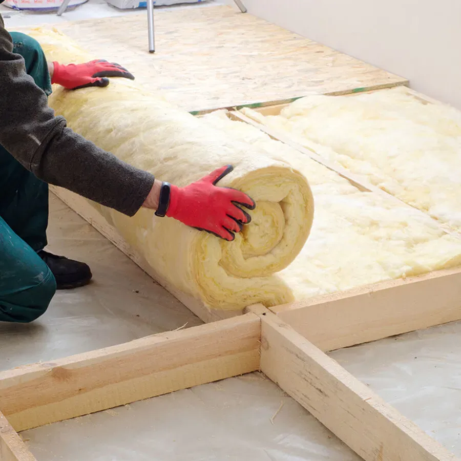 A person wearing red gloves is holding a roll of insulation.